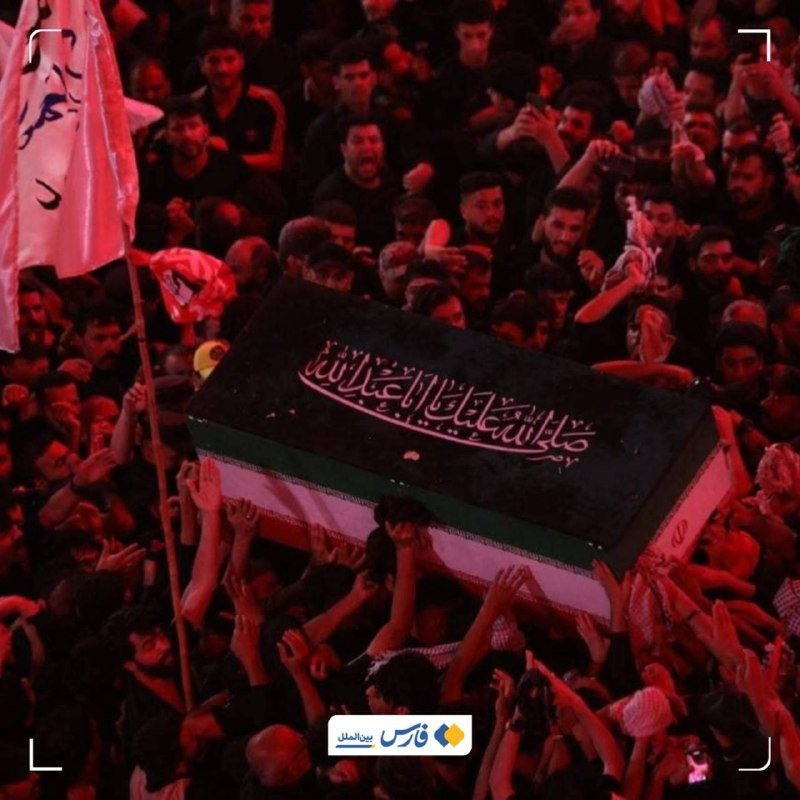 A dense crowd of mourners carries a black-draped casket with Arabic inscriptions on their shoulders and hands during a nighttime gathering.