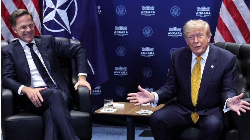 Two men in dark suits sit in black armchairs gesturing during a meeting, with a backdrop featuring NATO emblems and "Ankara Summit" text.