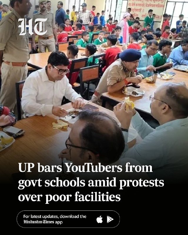 Men in uniform and civilian clothes sit at long tables eating meals alongside children in red and green shirts inside a crowded dining hall, with a "Hindustan Times" headline overlay.