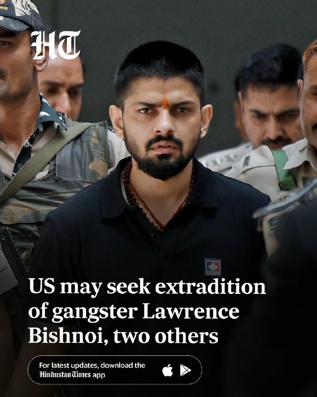 A bearded man in a black shirt with a forehead mark is escorted by uniformed personnel, with a news headline reading "US may seek extradition of gangster Lawrence Bishnoi, two others."