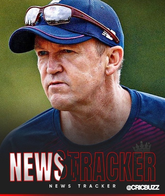 A middle-aged man in a blue cap with sunglasses perched on top and a dark blue shirt looks off-camera, overlaid with a "NEWSTRACKER" graphic and "@CRICBUZZ."
