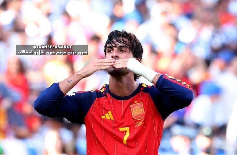 A soccer player in a red Spain jersey (number 7) covers his mouth while kissing his hand, with a blurred crowd in the background and Arabic text overlaid on the image.