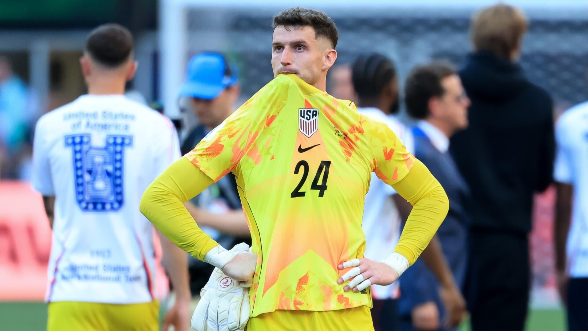 A soccer player wearing a navy USA #20 jersey with red trim runs on the field during a match, with blurred spectators visible in the background stands.