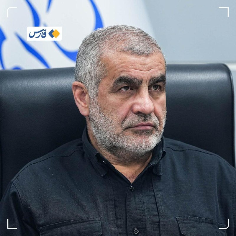 A gray-haired, bearded man in a dark shirt sits in a black leather chair with a partial emblem visible in the background.