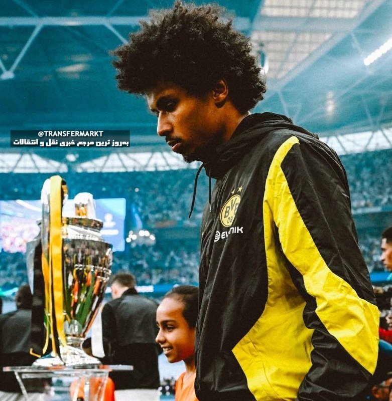 A soccer player in a white Real Madrid jersey with "Emirates Fly Better" sponsorship celebrates with an open-mouthed shout in a packed stadium.