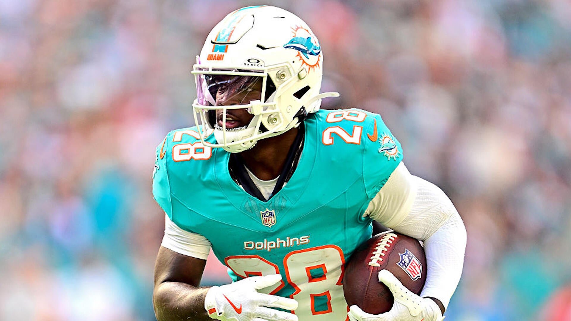A Miami Dolphins football player wearing jersey number 28 runs with the ball tucked under his arm during a game.