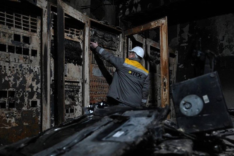 A worker in a hard hat and dark jacket labeled "UTEK" inspects heavily burned, charred server racks amid debris inside a fire-damaged facility.