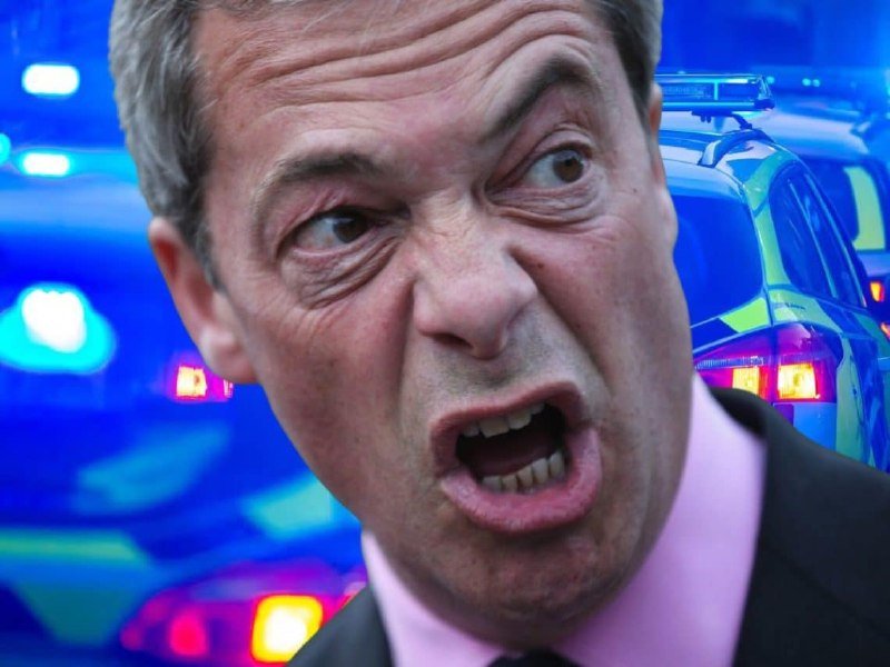 A man with gray hair, wearing a pink shirt and dark jacket, shouts with an open mouth in front of blurred blue emergency vehicle lights.