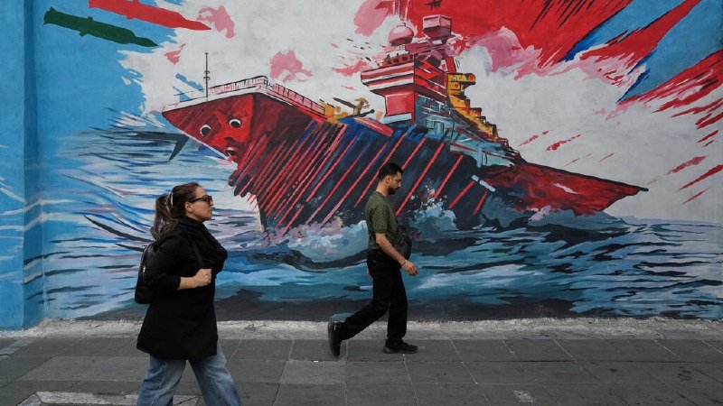 Two pedestrians walk past a large street mural depicting a red warship with a face on its hull sailing through stylized waves.