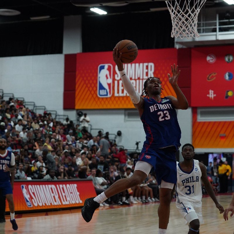 A Detroit basketball player wearing jersey number 23 leaps toward the hoop with the ball during an NBA Summer League game in front of a crowded arena.