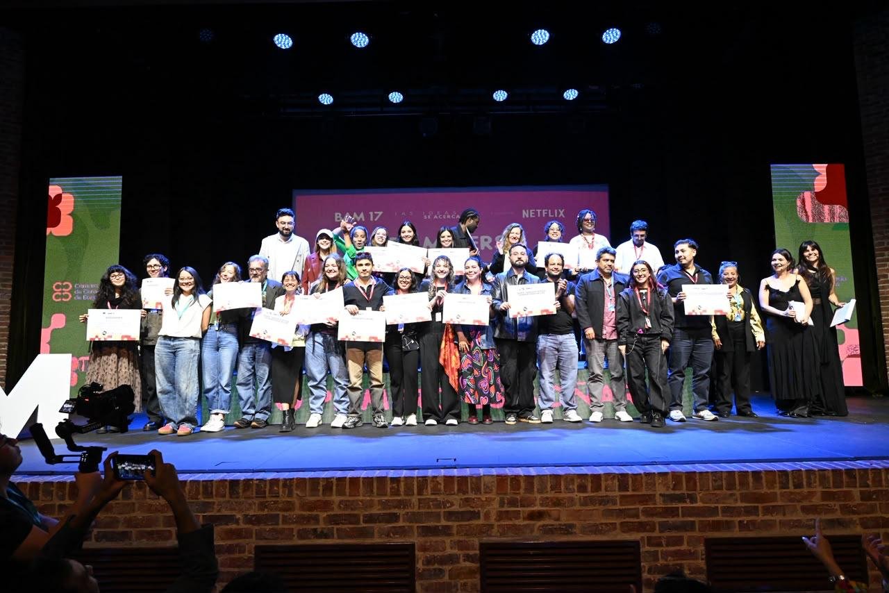 A large group of people stands on a stage holding certificates in front of a screen displaying "BAM 17" and "NETFLIX" logos, with a photographer in the foreground.