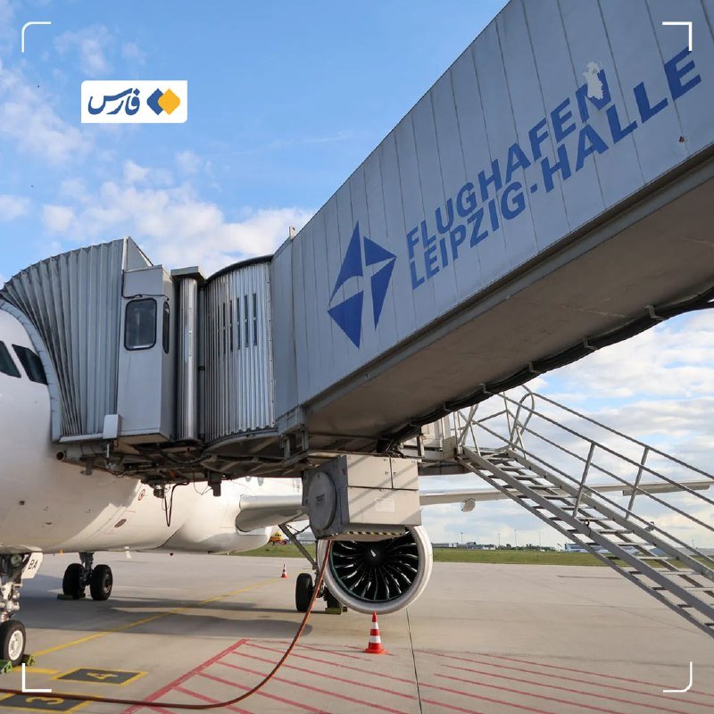 A white commercial airplane is connected to a jet bridge labeled "FLUGHAFEN LEIPZIG-HALLE" on the tarmac, with stairs descending to the ground.