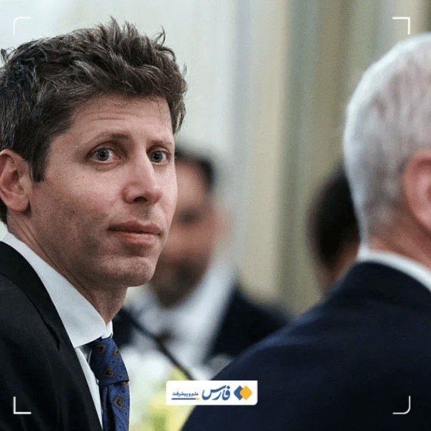 A man in a dark suit and tie stands in a crowded indoor setting, gazing toward a gray-haired man whose back is to the camera.