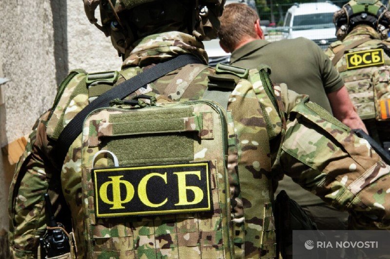 Personnel in camouflage uniforms with "ФСБ" patches walk outdoors near vehicles, with a "RIA Novosti" watermark visible.