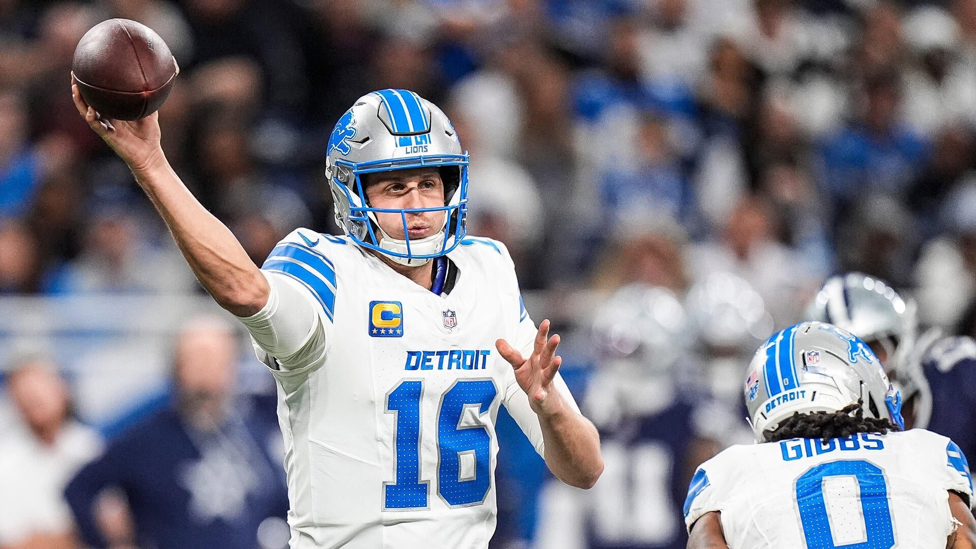 Detroit Lions quarterback #16 throws a pass during an NFL game, with teammate #0 (Gibbs) nearby and players in blue visible in the background.