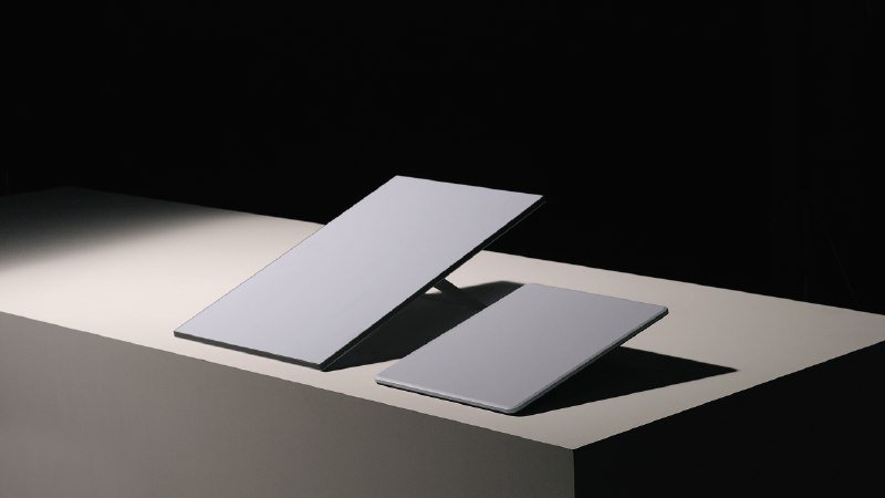 Two white electronic tablets rest on raised stands on a light-colored surface against a black background.