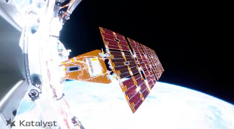 A spacecraft component with rectangular solar panel arrays floats above Earth's curvature against the blackness of space.