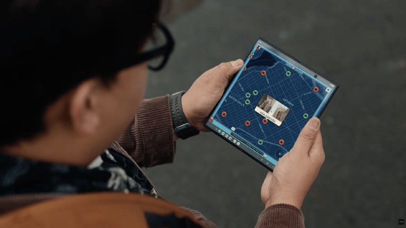 A person wearing glasses holds a foldable smartphone displaying a map interface with location markers and a small image overlay.