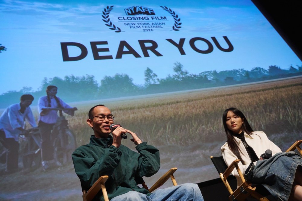 Two people sit in director's chairs on stage at the NYAFF 2022 Closing Film event for "Dear You," with one speaking into a microphone and a film scene projected behind them.