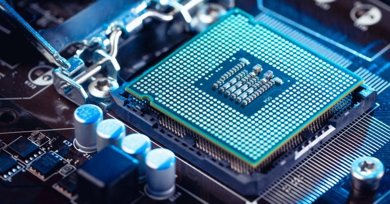 A metallic lever holds a square, pin-covered central processing unit seated in a motherboard socket, illuminated by blue lighting.