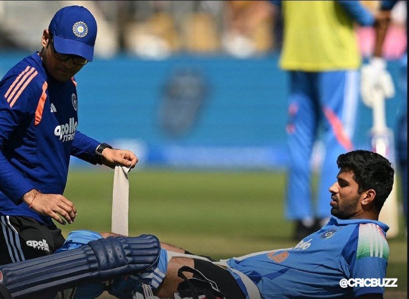 A man in a blue cap and "Apollo Tyres" jersey wraps an ankle bandage around a seated cricketer wearing batting pads during what appears to be a training session on a grass field.