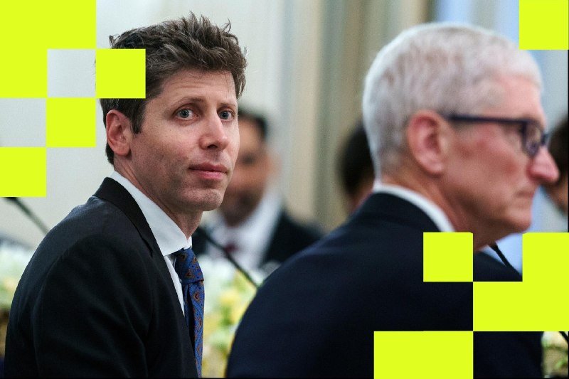 A dark-haired man in a suit looks over his shoulder while a gray-haired, bespectacled man sits beside him at a formal gathering.