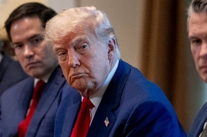 An older man with blonde hair wearing a blue suit and red tie looks downward with a serious expression, flanked by other suited men in a formal setting.