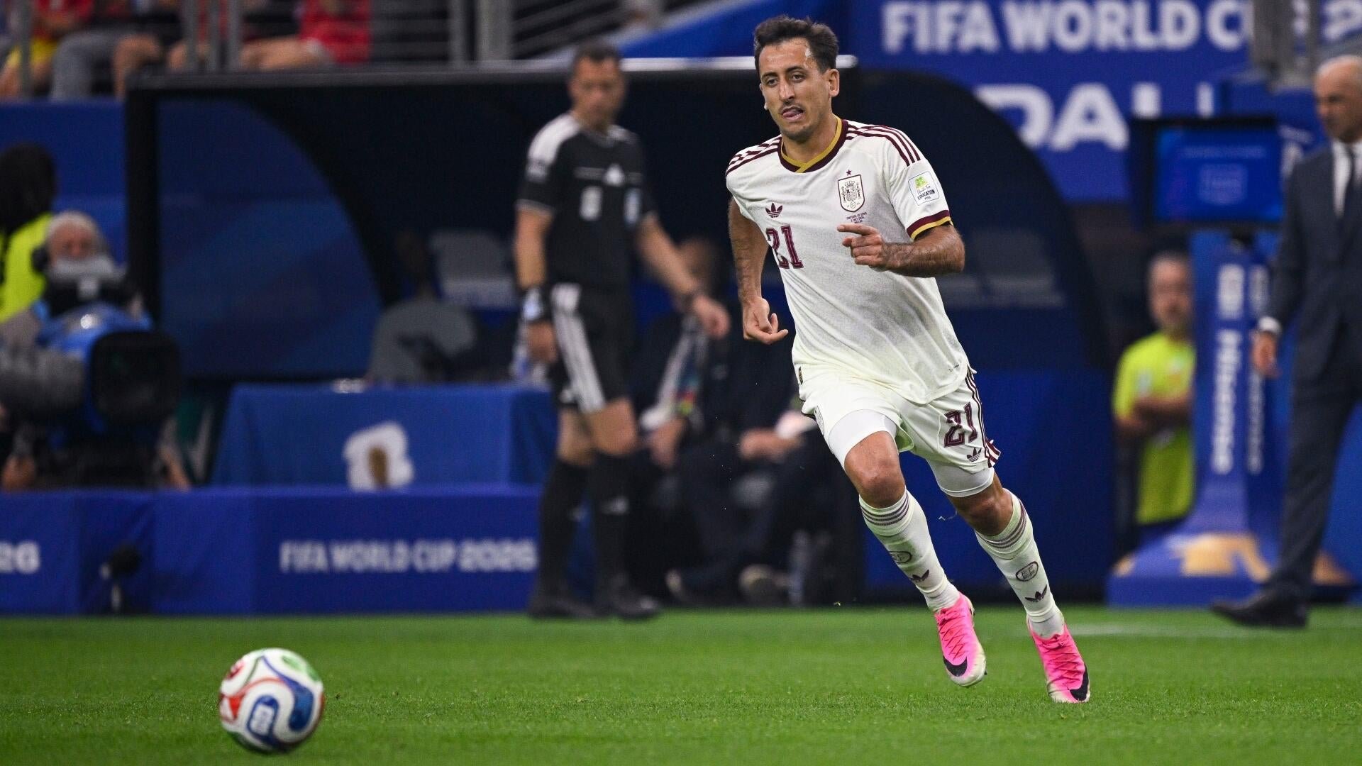 A soccer player in a white uniform with the number 21 runs toward a ball during a FIFA World Cup 2026 match on a grass field.