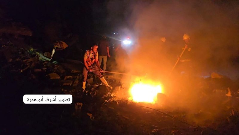 Rescue workers use a hose and headlamps to extinguish a fire amid rubble at night.