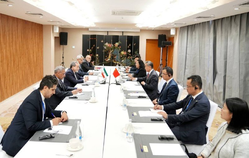 Two delegations in business attire sit facing each other across a long conference table with Iranian and Indonesian flags placed at its center.