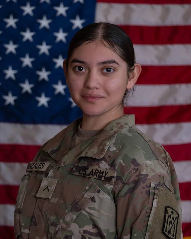 A female U.S. Army soldier wearing a camouflage uniform with "GONZALES" and "U.S. ARMY" name tapes stands in front of an American flag.