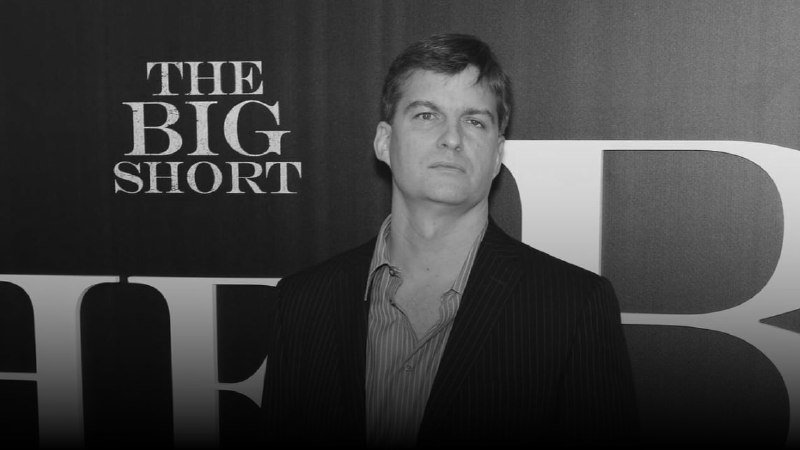 A man in a dark blazer and striped shirt stands at a promotional event, with "THE BIG SHORT" logo visible in the background.