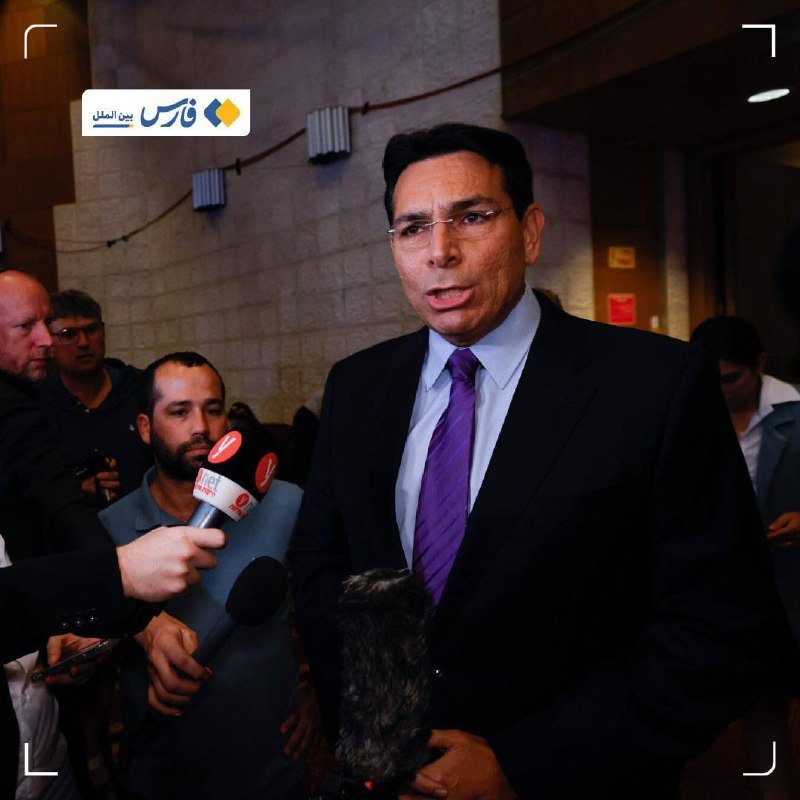 A man in a dark suit and purple tie speaks to reporters holding microphones inside a stone-walled building.