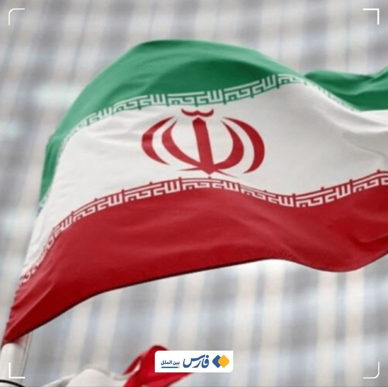 The Iranian flag, featuring green, white, and red horizontal stripes with a central red emblem, waves against a blurred background.