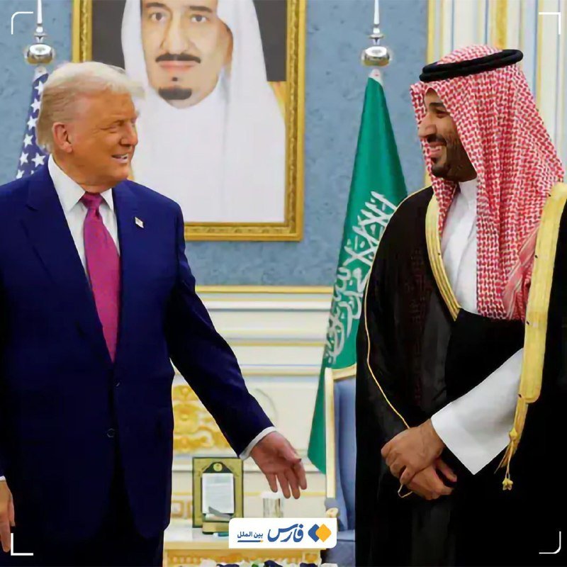 Two men smile and reach toward each other in a formal meeting room, with an American flag, a green flag, and a large framed portrait visible in the background.