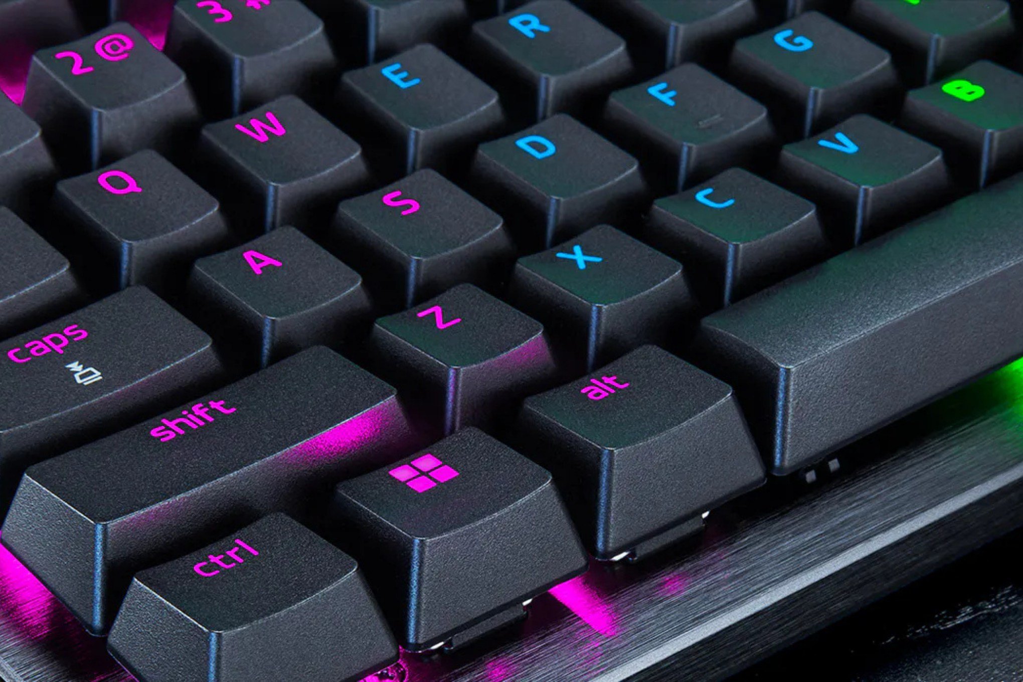 Close-up of a black backlit gaming keyboard with pink and cyan illuminated keys including shift, ctrl, alt, caps, and the Windows logo.
