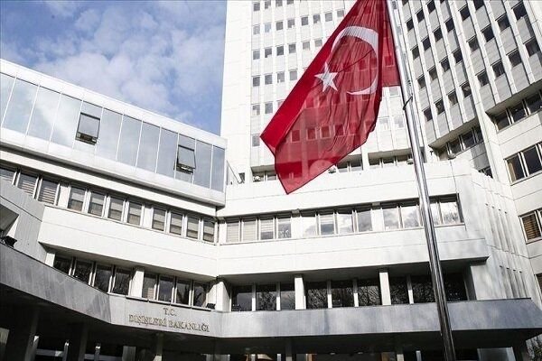 A Turkish flag flies in front of a modern multi-story white building with "T.C. DIŞİŞLERİ BAKANLIĞI" inscribed above its entrance.