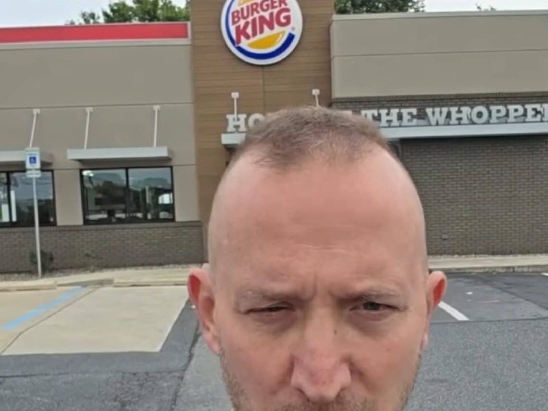 A close-up shows a man's head and face in the foreground, with a Burger King restaurant featuring its logo and signage in the background.