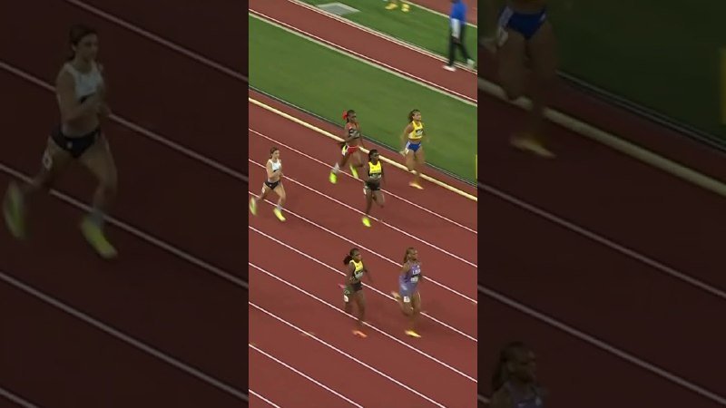 Female athletes compete in a track race on a red running track, with a grassy infield visible in the background.