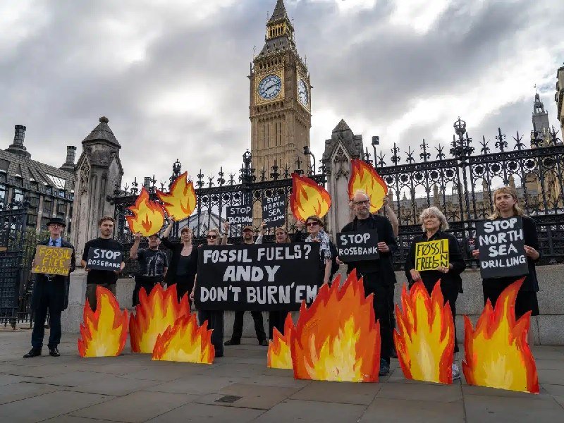 Protesters holding flame cutouts and signs reading "FOSSIL FUELS? ANDY DON'T BURN 'EM," "STOP ROSEBANK," and "STOP NORTH SEA DRILLING" stand before Big Ben in London.