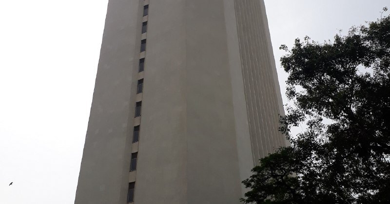 A tall, light-colored high-rise building rises against an overcast sky, with green tree foliage visible on the right side.