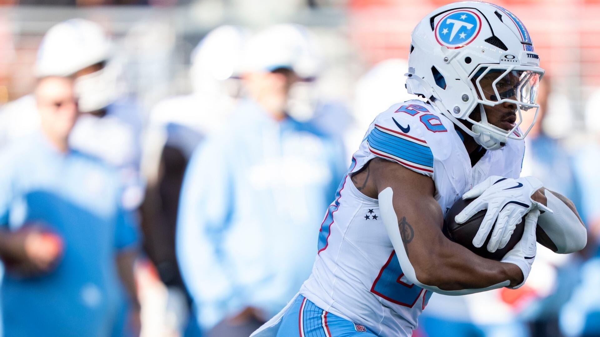 A football player in a white and light blue Titans uniform runs with the ball tucked under his arm during a game.