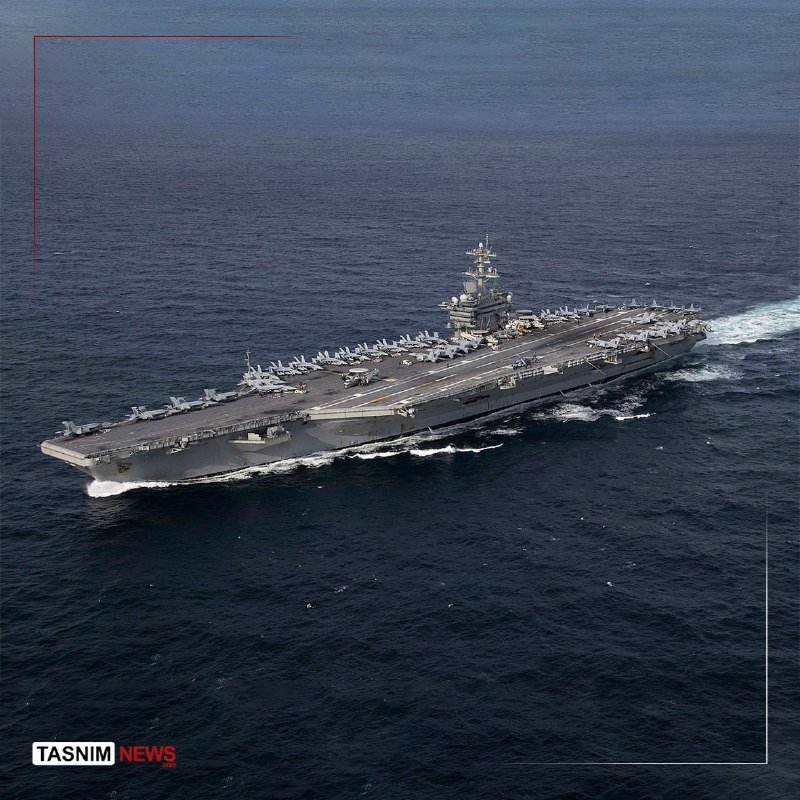 A large aircraft carrier with multiple jets parked on its deck sails through dark blue open water.
