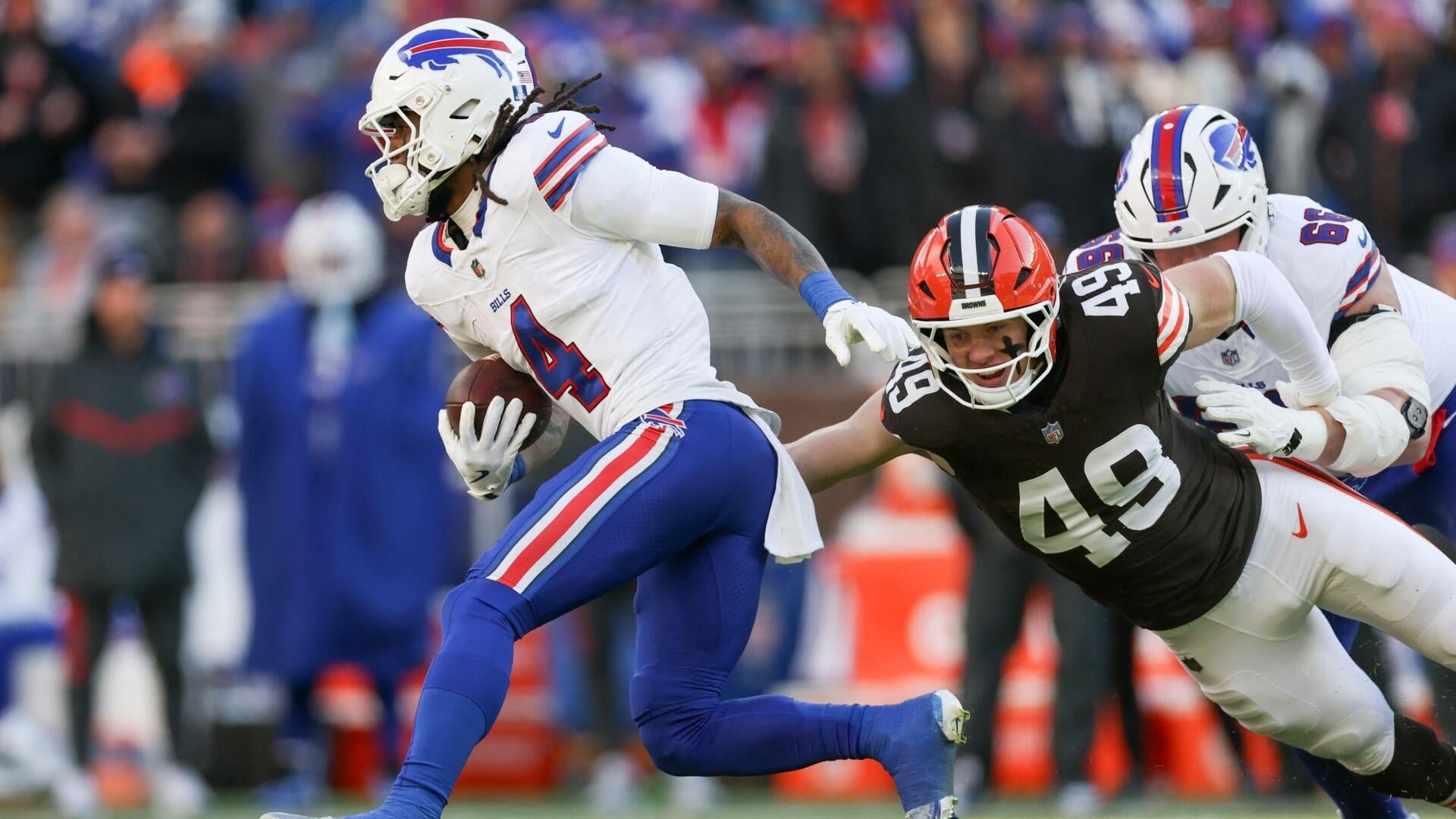 A Bills running back carrying the football stiff-arms a Browns defender wearing number 49 during an NFL game, with a blurred crowd in the background.