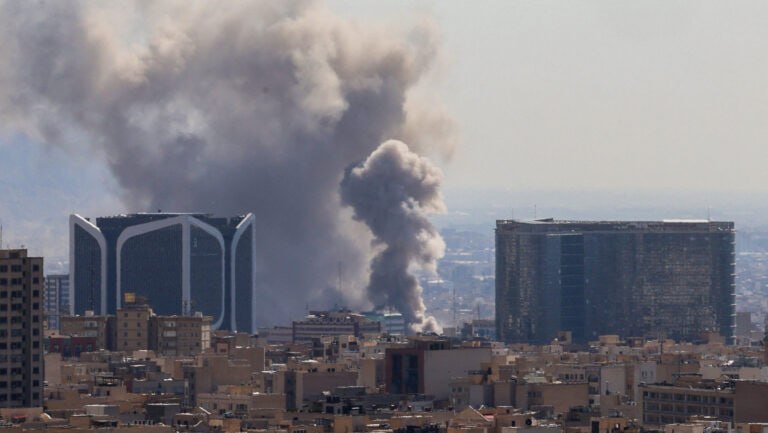 Large plumes of gray and white smoke rise from a densely packed city skyline.