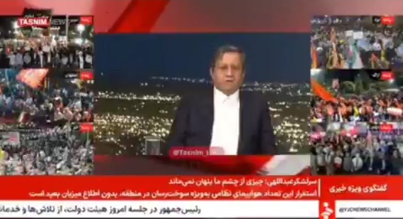 A male news anchor in a dark suit presents a broadcast against a nighttime cityscape backdrop, flanked by side panels showing large outdoor crowds holding flags.