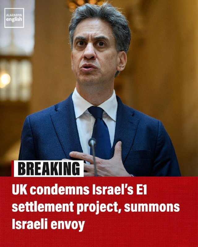 A man in a dark suit and tie speaks into a microphone, with an Al Arabiya English logo and a "BREAKING" banner reading "UK condemns Israel's E1 settlement project, summons Israeli envoy."