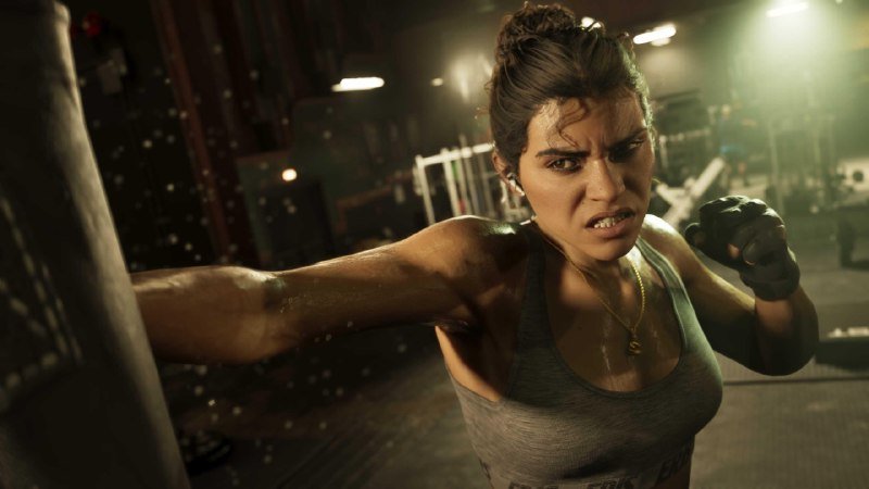 A sweaty woman in a gray tank top throws a punch at a heavy bag in a dimly lit gym, wearing fingerless gloves and a determined expression.