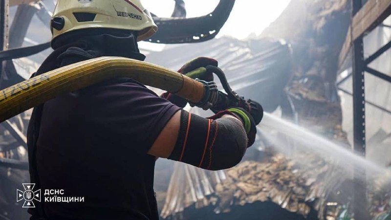 A firefighter in a helmet and protective gear sprays a water hose onto the smoldering wreckage of a building's collapsed roof and walls.