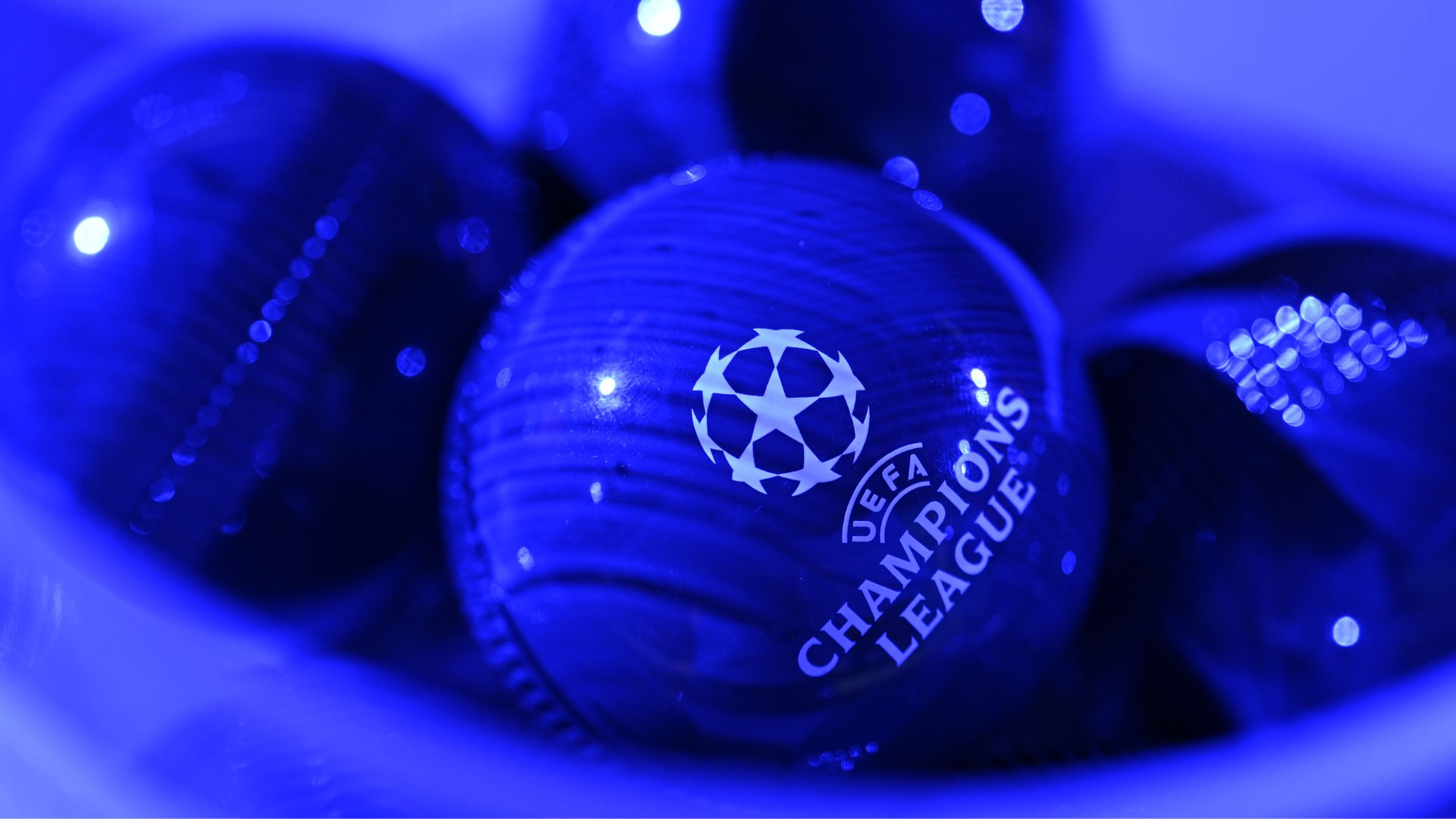 A blue UEFA Champions League match ball rests on blue fabric, illuminated by blue lighting.